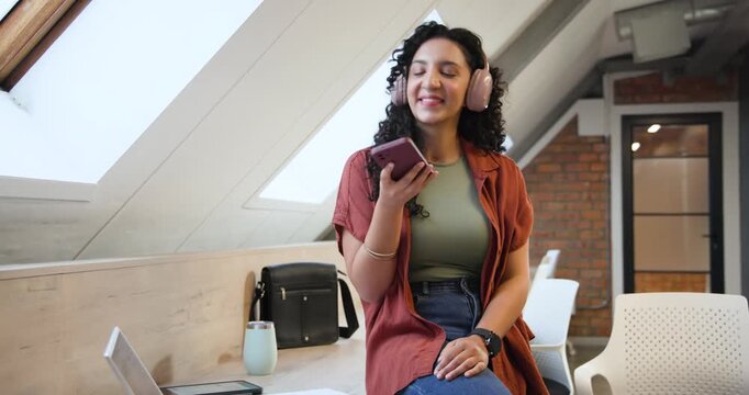 African American woman adjusting pink headphones, tapping purple phone in loft, recording message
