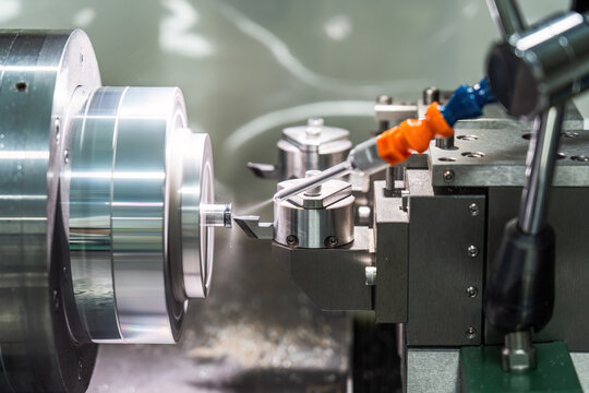 A metal lathe performs precision cutting on a cylindrical workpiece, with coolant spraying during the industrial machining process.