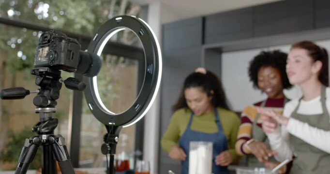 Diverse female friends in aprons filming after camera rig, measuring and whisking on kitchen island
