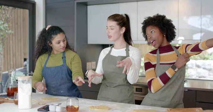 Diverse women friends in aprons starting with dough discs, shaping and sharing tips in kitchen