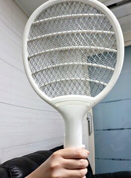 Hand holding a rechargeable electric fly swatter indoors