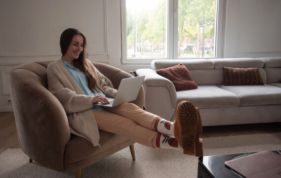 Relaxed young woman using laptop with feet up at home