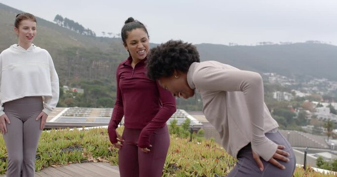 Female coach wearing burgundy guiding hip moves on rooftop deck to ease woman holding lower back