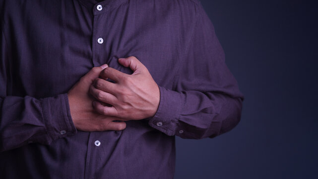Adult man experiences severe chest pain and a potential heart attack, tightly holding his heart in medical distress. This health illness and disease causes intense pain and stress.