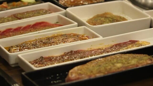 A close-up video of raw beef slices marinated with spices, seasonings, and sauce in a tray, ready for grilling in a restaurant kitchen or grilling area.