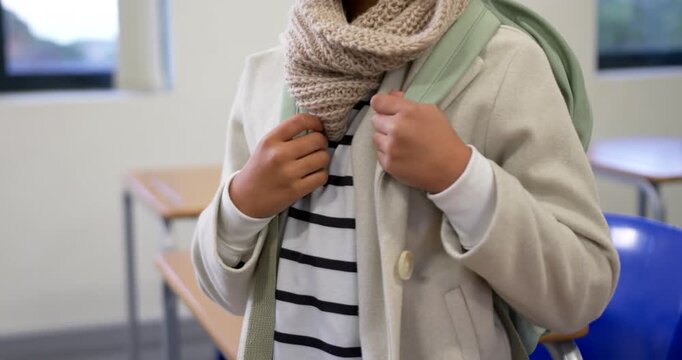 African American teen girl adjusting mint backpack straps, beige scarf preparing to leave classroom