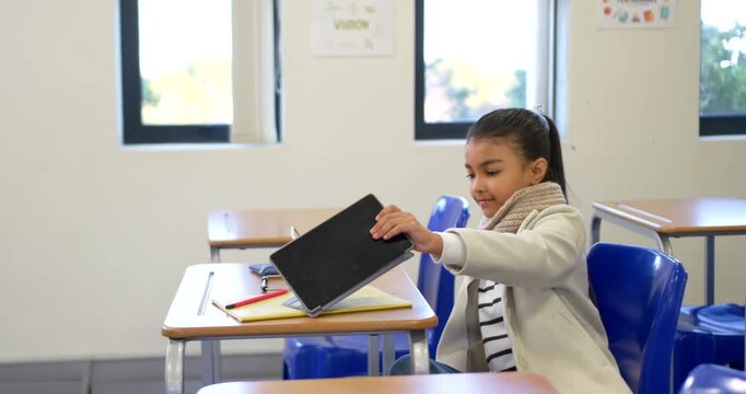 African American teen reaching, rotating tablet case in class at desk, viewing screen for class