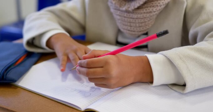 African American youth student prompted by task writing in notebook with pink pencil at school desk