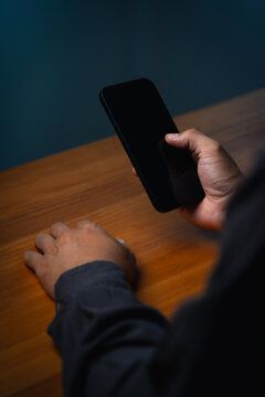 Adult man using a blank smartphone screen mockup over a wooden table. Hand holding modern technology for business communication, internet connection, and digital networking online.