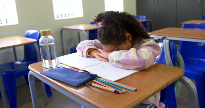 Teenage student resting on folded arms at school desk after opening notes to rest, camera moving