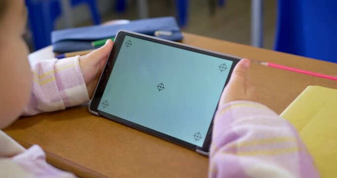 Teenage African student seeing markers, steadying and tilting tablet to view screen at school desk