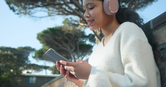 Child female sitting on park bench looking down and tapping tablet, engaging, with pink headset