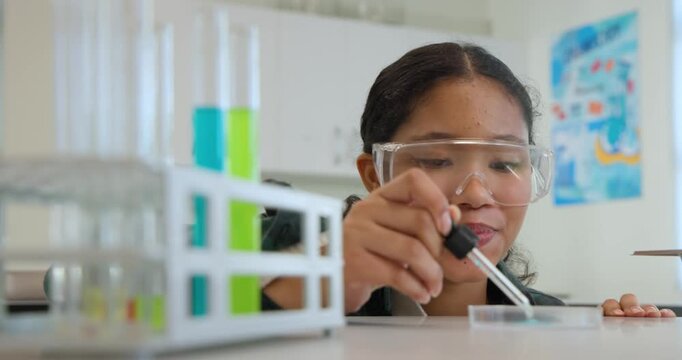 Child leaning with goggles squeezing dropper studying blue liquid spreading in petri dish in lab