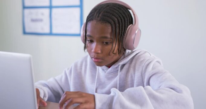 African American male youth typing on silver laptop, opening notebook, writing with pen, studying