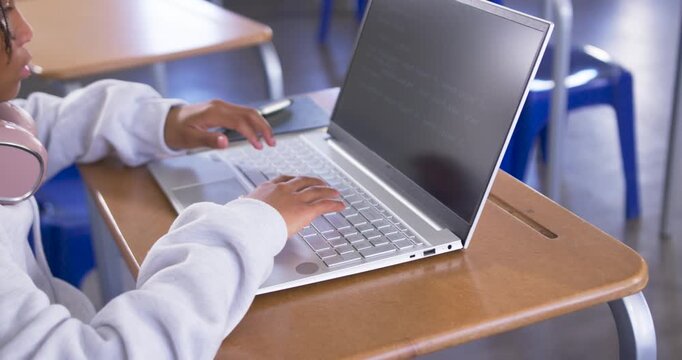 African American teenage male approaching from left, typing on silver laptop at school for homework