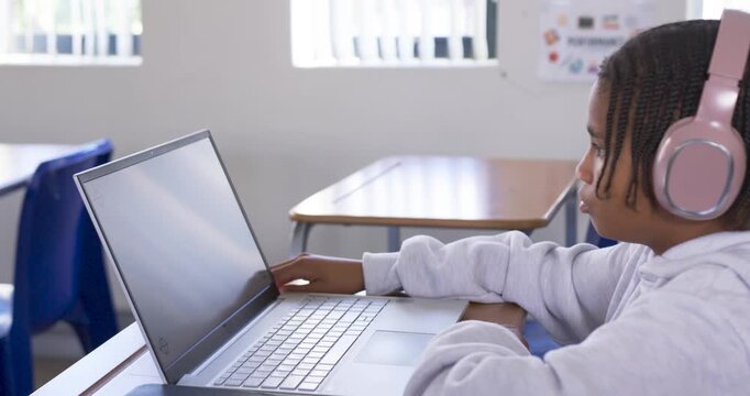 African American youth reaching for laptop trackpad with pink headset, studying at desk, copy space