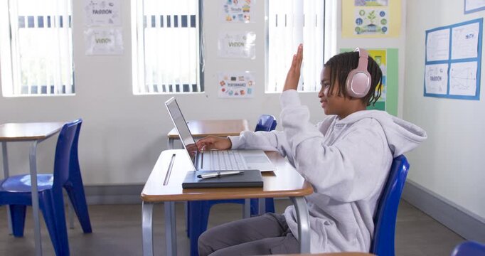 African Youth raising hand, answering laptop prompt, sipping blue bottle at school desk, copy space
