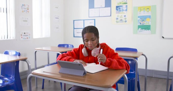 African American teenage student in red hoodie using tablet, grabbing pen, taking notes at school