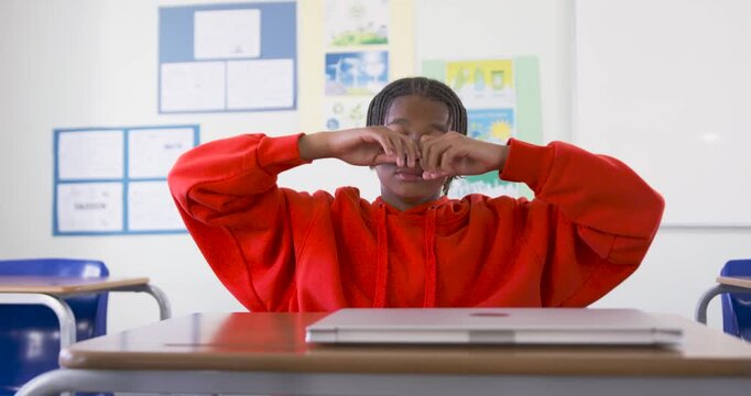 African American teen male at desk waking rubbing eyes stretching opening silver laptop for class