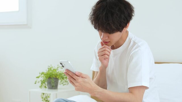 悩みながらスマートフォンを使う若い男性
