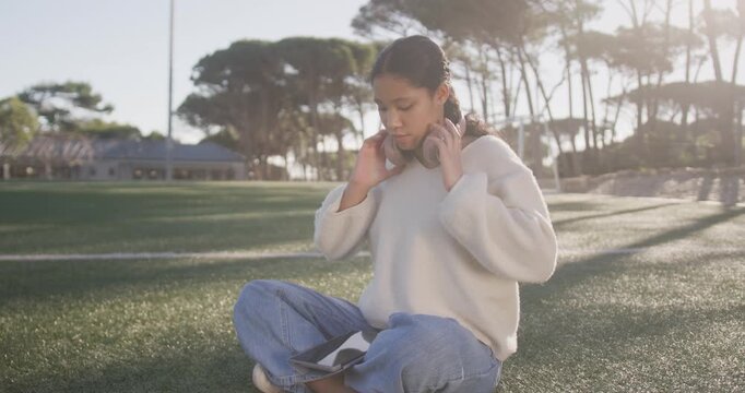 School-age girl putting pink headset, reading tablet, tucking it, standing, walking on grass