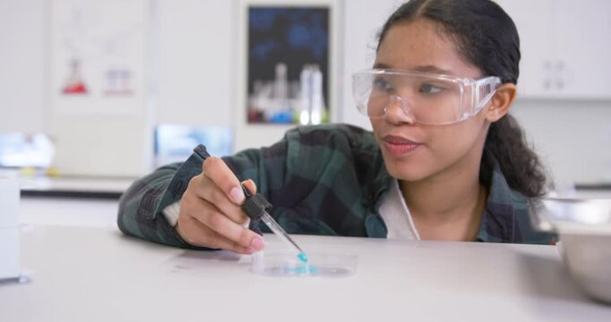 Child female student following lesson, using dropper adding blue reagent into test tubes in lab