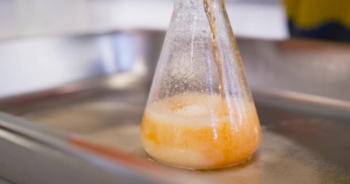 Clear conical flask producing creamy orange foam after reagent pouring on metal tray for demo
