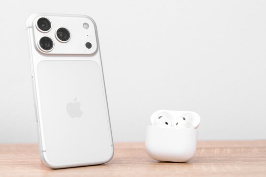Bar, Montenegro: February 6, 2026: White apple iphone 17 pro standing beside open wireless earbuds case on wooden table by grey wall, new audio technology delivery concept