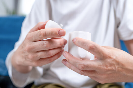 Person holding a round white medical sensor applicator with both hands while seated indoors before attaching it to the skin to determine insulin in the blood