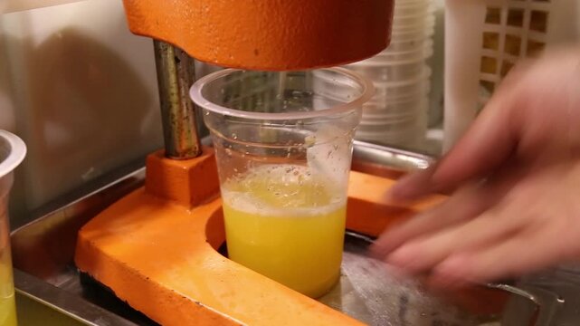 Close-up video of freshly squeezed citrus juice dripping from a manual press into a clear cup, showing a refreshing natural beverage preparation process.
