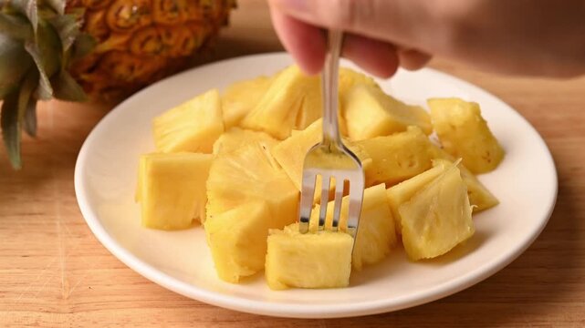 Close up of woman hands using a fork to pick up a sliced fresh pineapple from a plate to eat