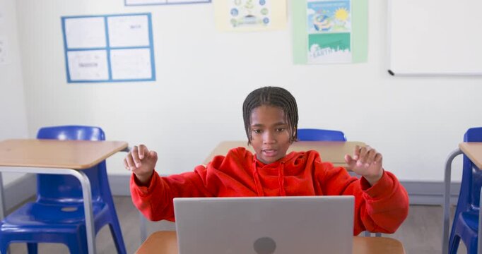 African American teen in red hoodie stretching, opening laptop, aligning lid, resting head on desk