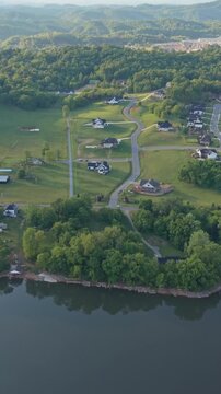 Vertical screen. Aerial perspective of suburban area in Johnson City, Tennessee, highlighting curving streets, spacious yards houses surrounded by lush greenery and rolling hills under bright daylight