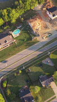 Vertical screen. Aerial perspective of a suburban area in Johnson City, Tennessee, featuring residential houses, an active construction site, and a road lined with trees and manicured lawns