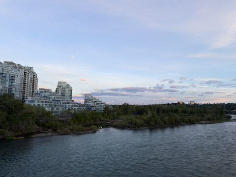 Bow River flowing past residential condominium buildings under a morning sky in Calgary