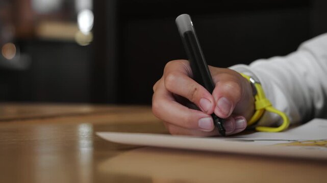 Close-up of a child drawing with a black marker on paper at a wooden table. Creative learning, education and childhood development concept.