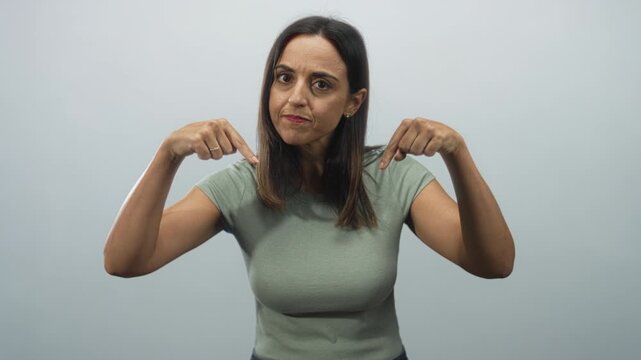 Woman pointing fingers at her chest in studio, frowning with raised brows and expressive hands while asking who me gesture; self doubt.