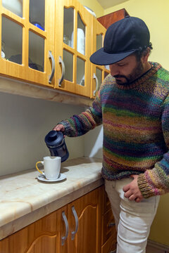 Man in sweater making fresh coffee in a French press press in his kitchen