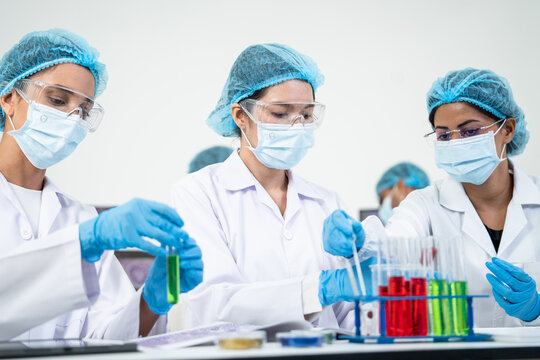 Group of researcher carrying out chemical solution test with glass tube rack during biotechnology laboratory experiment