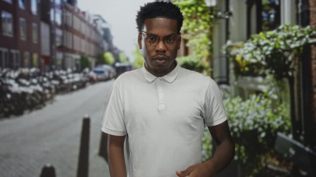 Man with glasses walks on a busy bustling urban street lined with multistory buildings and parked bicycles; confidence.