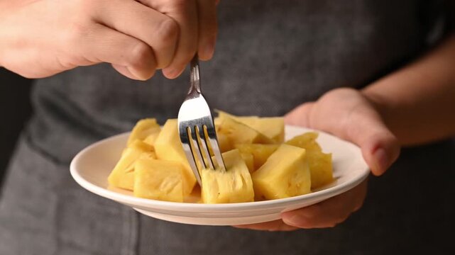 Close up of woman hands holding plate of sliced pineapple and using a fork to eat