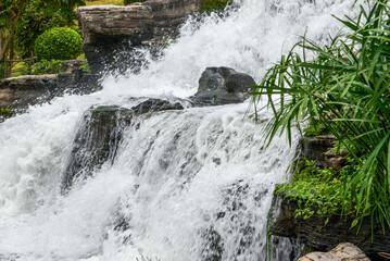 Garden waterfall flowing beside green plants and cascading rocks © Steve