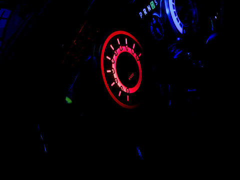 Glowing red dashboard dial illuminated in the dark interior of a car.