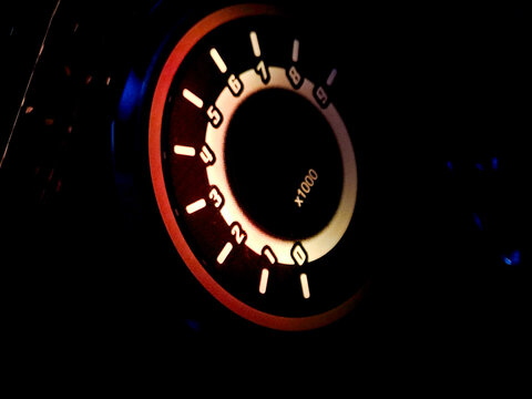 Glowing car tachometer dashboard dial in dark night interior.