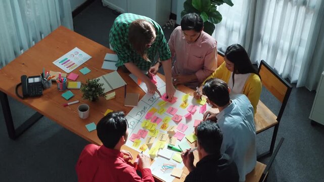 Close up of professional business team hands writing and putting sticky note on scrum task board. Top view of project manager write task and use kanban board to manage time and workflow. Convocation.
