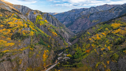 Obraz premium Aerial view of Colorado mountains canyon fall foliage trees along Million Dollar Highway and car travel on winding road during autumn season near Ouray amongst San Juan Mountains landscape