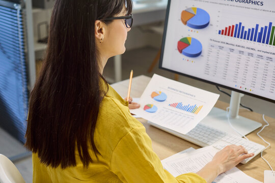 Woman analyst reviews finance data charts in office. She works at a computer monitor, comparing graphs and reports to plan budgets and forecasts. Concept is financial analysis and reporting.