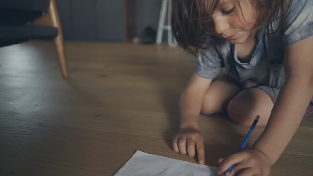 Focused child drawing with a blue pencil on the floor