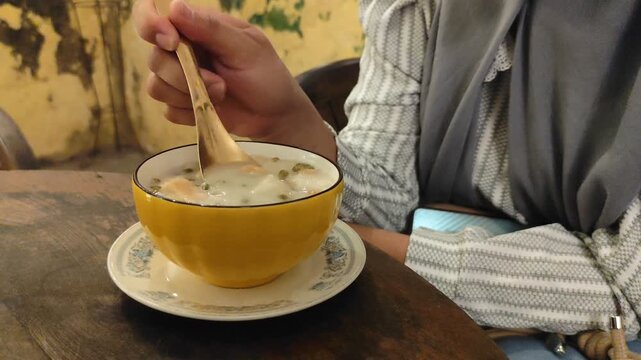 A woman is eating Angsle, a traditional dish from Javanese, Indonesia. Angsle It offers a delicious flavor profile, blending a warm coconut milk broth and the aroma of ginger.
