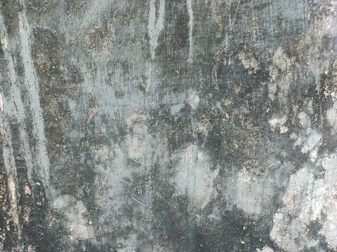 A weathered outdoor concrete wall displays faded grey paint, peeling plaster, dark mold stains, rough textures, and signs of age.